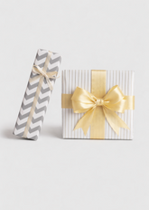 Gift wrapping option: two wrapped gift boxes in grey chevron and white striped paper with gold satin ribbon bows