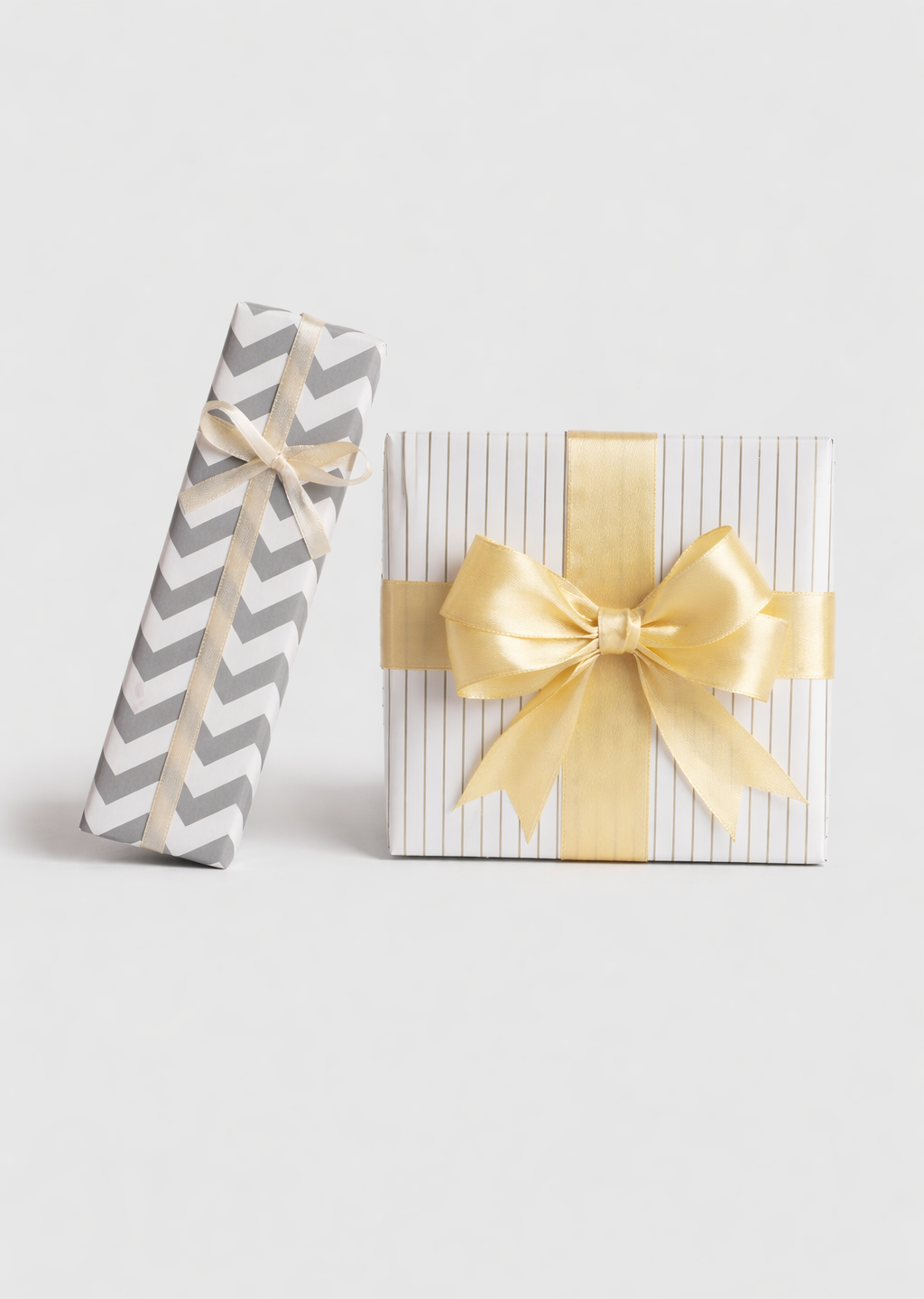Gift wrapping option: two wrapped gift boxes in grey chevron and white striped paper with gold satin ribbon bows